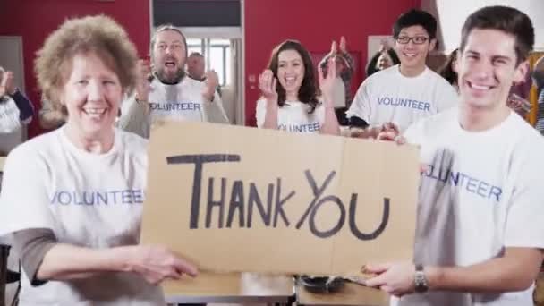 Two Charity workers hold up a Thank you sign as their fellow workers applaud — Stock Video