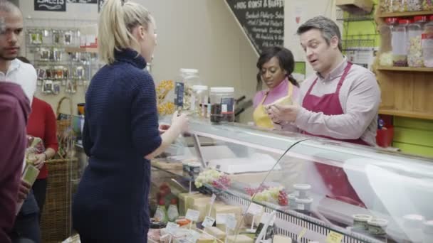 Vriendelijke delicatessen medewerkers bedienen van klanten met een glimlach aan de balie van kaas — Stockvideo