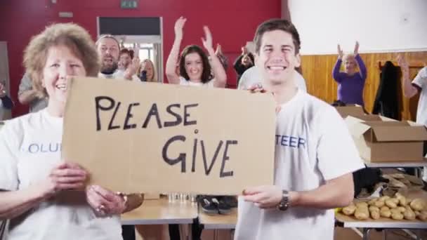 Two Charity workers hold up a Please Give sign as their fellow workers applaud — Stock Video