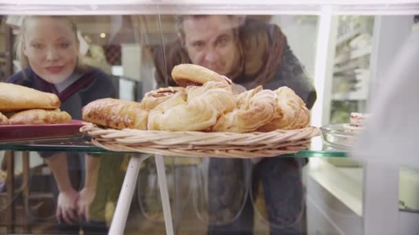 Des clients heureux regardant à travers une armoire en verre et choisissant des pâtisseries fraîches — Video