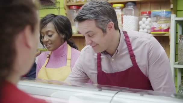 Friendly delicatessen staff serving customers with a smile at the cheese counter — Stock Video