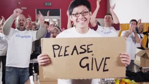 Charity worker holds up a Please Give sign as his fellow workers applaud — Stock Video