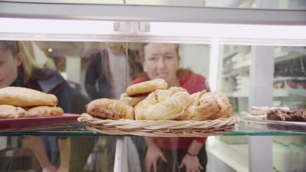 Clientes felices mirando a través de un gabinete de vidrio y eligiendo pasteles frescos — Vídeos de Stock