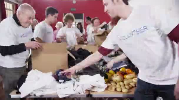 Gran grupo de voluntarios de caridad que clasifican entre los bienes donados — Vídeo de stock