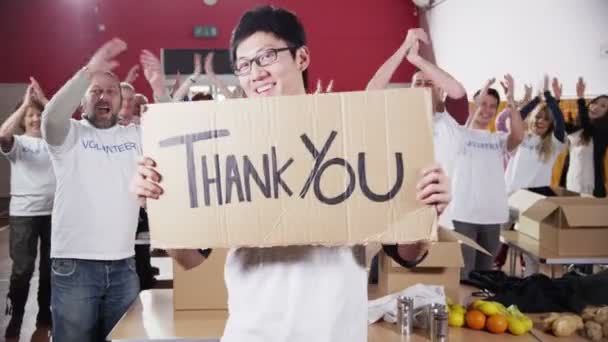 Благодійний працівник тримає підпис спасибі, як його колеги аплодують — стокове відео