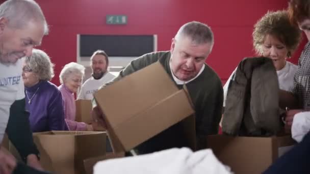 Trabajadores de la caridad y miembros de la comunidad clasifican a través de pilas de ropa donada — Vídeos de Stock