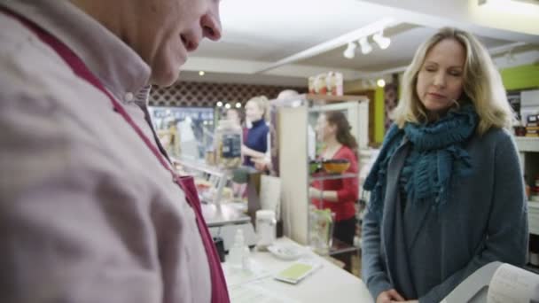 Winkelier neemt een credit card betaling van een vrolijke vrouwelijke klant — Stockvideo