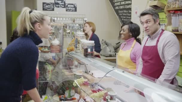 Friendly delicatessen staff serving customers with a smile at the cheese counter — Stock Video