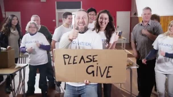 Group of charity volunteers give thumbs up to camera with a Please Give sign — Stock Video