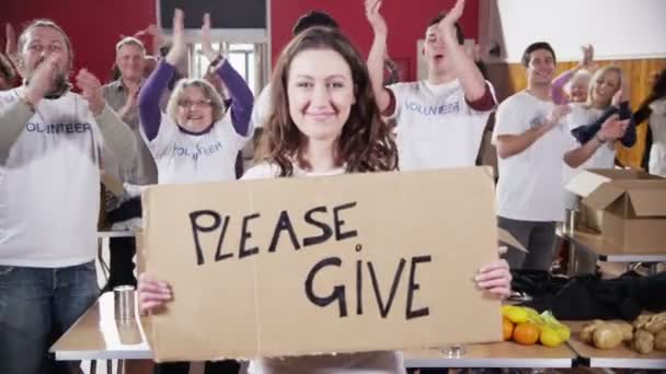 Charity worker holds up a Please Give sign as her fellow workers applaud — Stock Video