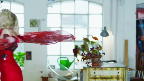 Mujer joven en un vestido rojo girando y bailando alrededor de su apartamento — Vídeos de Stock
