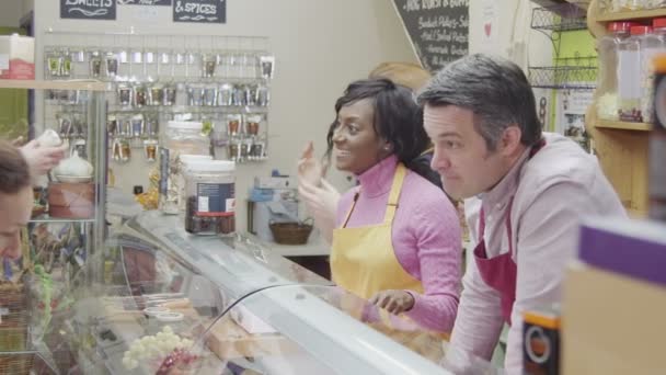 Friendly delicatessen staff serving customers with a smile at the cheese counter — Stock Video