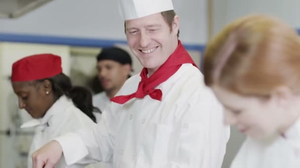 Equipe feliz de chefs na cozinha comercial, preparando comida e conversando juntos — Vídeo de Stock