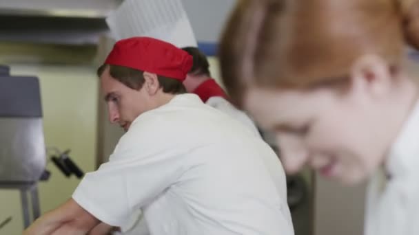 Equipe feliz de chefs na cozinha comercial, preparando comida e conversando juntos — Vídeo de Stock