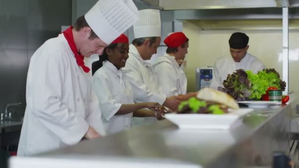 Equipo feliz de chefs preparando y cocinando comida en una cocina comercial — Vídeo de stock