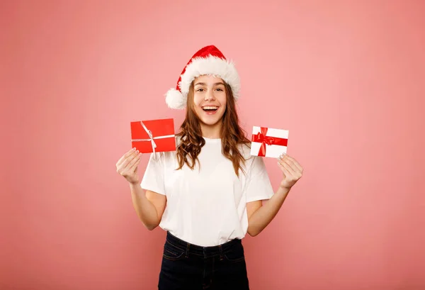 快乐的高加索女孩 身穿白色T恤 头戴红帽 手持两张礼券 或带着粉色背景的贺卡 站在那里 工作室肖像 圣诞及新年假期概念 — 图库照片