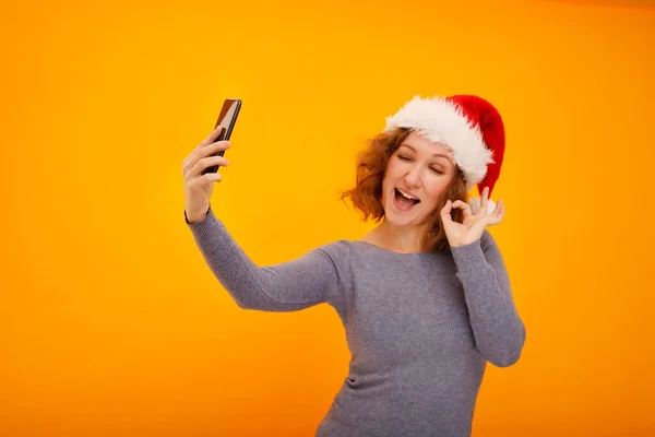 Sarı Arka Planda Duran Noel Baba Şapkalı Kıvırcık Saçlı Selfie — Stok fotoğraf