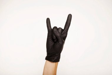 El, siyah tıbbi eldivenlerle beyaz arka planda izole edilmiş şeytan boynuzları gösteriyor. Kaya işareti.