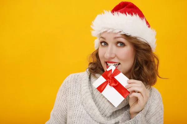身穿白色冬季毛衣 头戴红色圣诞老人帽的快乐的年轻女性持黄色橙色背景的礼券 人的生活方式概念 模拟复制空间 — 图库照片
