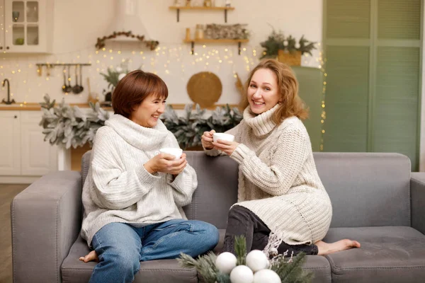 幸せな家族の母親を愛し 大人の娘はクリスマスに熱いお茶を楽しみ お互いに話をして飾られたキッチンに座っています クリスマスと新年のコンセプト — ストック写真