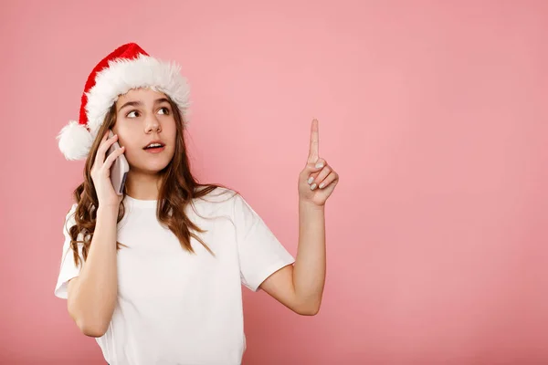 快乐的少女戴着圣诞爪帽在电话上聊天 手拉手在复制空间 快乐的女人喜欢愉快的移动对话 微笑的千禧女囚在粉色背景下通过电话交谈 图库图片