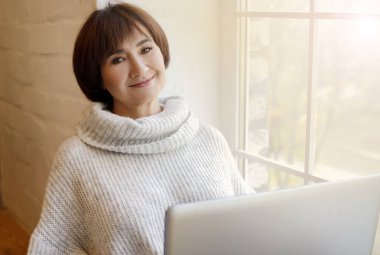 Bilgisayarında çalışan ya da öğrenen orta yaşlı bir kadın karantina altındaki oturma odasında oturmuş not defterine merhaba diyor. Sosyal uzaklık iletişimi