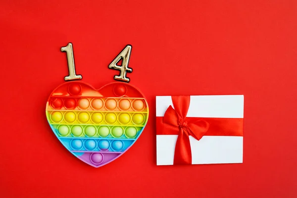 虹色のハートは その上に14番と赤い背景に赤い弓で白い証明書を持つストレス対策おもちゃを人気があります バレンタインデーのコンセプトのためのロマンチックな愛の手紙 テキストのスペース — ストック写真