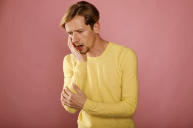 Pembe arka planda diş ağrısı olan sarı kazaklı genç beyaz bir adam. Diş hekimi sağlık hizmeti kavramı