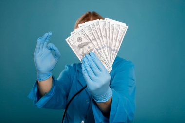 Dolarları tutan ve mavi arka planda koruyucu eldiven takan kadın doktor. Tıpta yolsuzluk ya da rüşvet kavramı