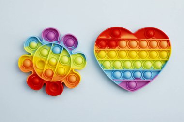 Rengarenk stres önleyici oyuncakların üst görüntüsü mavi arka planda gökkuşağı kalbi ve çiçeği ortaya çıkarır. Çocuk oyuncaklarının yaratıcı ve komik kavramları. Popüler oyuncak. Moda Oyuncağı 2021-2022.