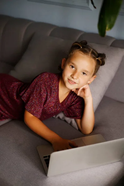 漂亮的少女躺在沙发上 手摸着脸颊 坐在笔记本电脑前 在线教育距离概念 — 图库照片
