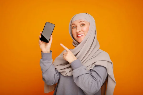 年轻快乐的穆斯林妇女用手机站在黄色背景上 用手指在智能手机上显示 自由科技生活方式穆斯林的概念 — 图库照片