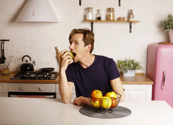 活泼的男人吃苹果时感到快乐 有魅力的年轻男性在家里的厨房里吃健康的食物 健康与减肥概念 图库照片