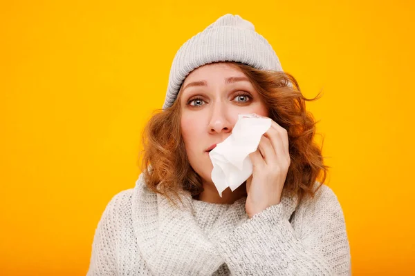 感冒的女人用组织吹她流鼻涕的鼻子 穿着冬季毛衣和帽子的漂亮姑娘因感冒打喷嚏而生病的画像 保健和医疗概念 图库图片