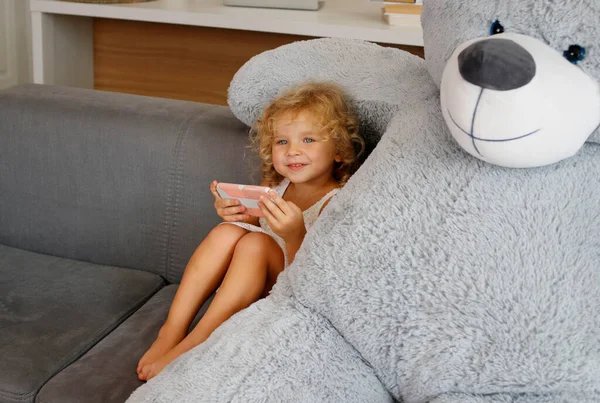 Cute Happy Little Girl Smartphone Sitting Sofa Big Toy Bear — стоковое фото