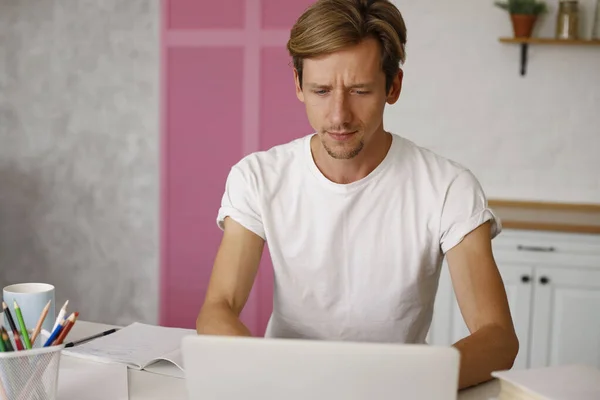 Young man freelancer using laptop studying online working from home, happy casual millennial guy typing on pc notebook surfing internet looking at screen enjoying distant job sit at table