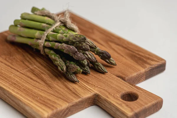 Güzel bir ahşap tahtanın üzerinde bir sürü taze kuşkonmaz yatıyor. dikey kare