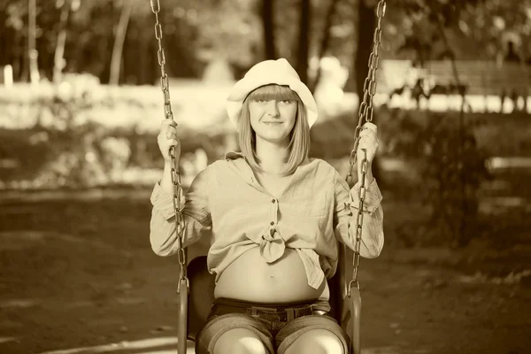 Beautiful pregnant woman sitting on a swing — Stock Photo, Image