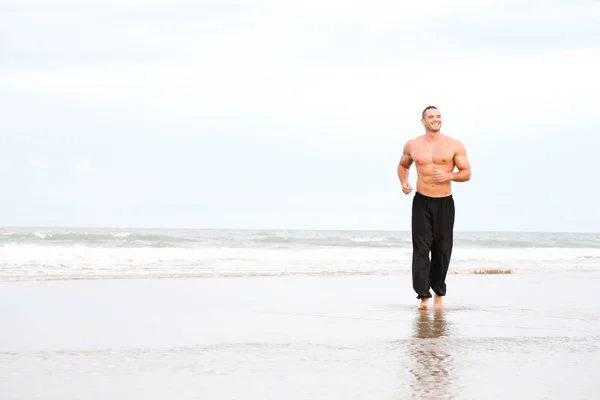 Junger schöner muskulöser Mann läuft am Strand — Stockfoto