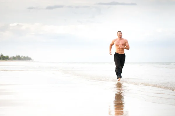 年轻英俊的肌肉男人在海滩上运行 — 图库照片