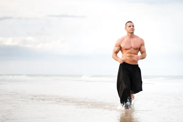 Körperlich fitter Mann läuft am Strand — Stockfoto