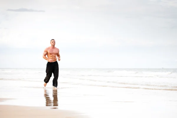 Junger schöner muskulöser Mann läuft am Strand — Stockfoto