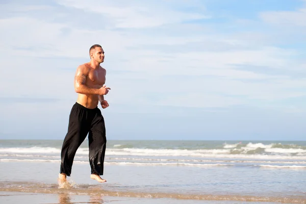 Junger schöner muskulöser Mann läuft am Strand — Stockfoto