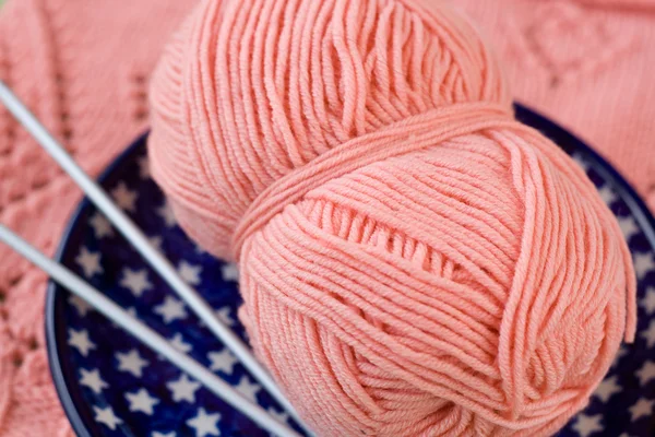 Une boule de fil rose et des aiguilles à tricoter sur une assiette bleue — Photo