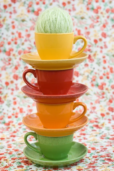 Четыре разноцветные чашки и клубки пряжи на фоне красного цветка — стоковое фото