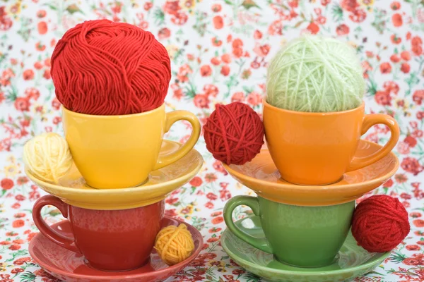 Quatro copos coloridos e bolas de fio em um fundo de uma flor vermelha — Fotografia de Stock