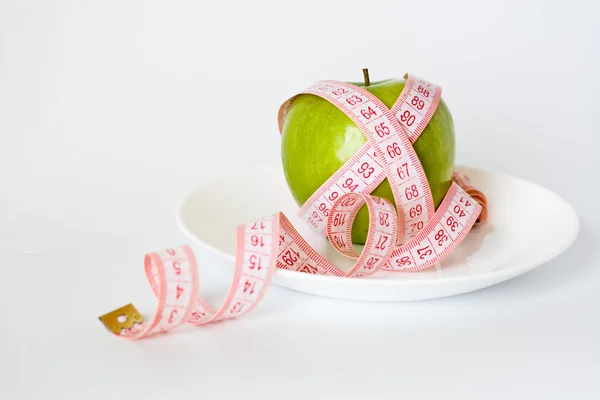 Green apple and measuring tape on a white plate — Stock Photo, Image