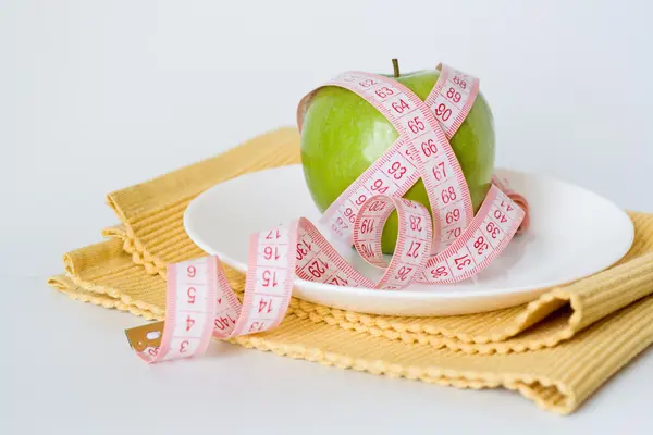 Groene appel en meetband op een witte plaat — Stockfoto