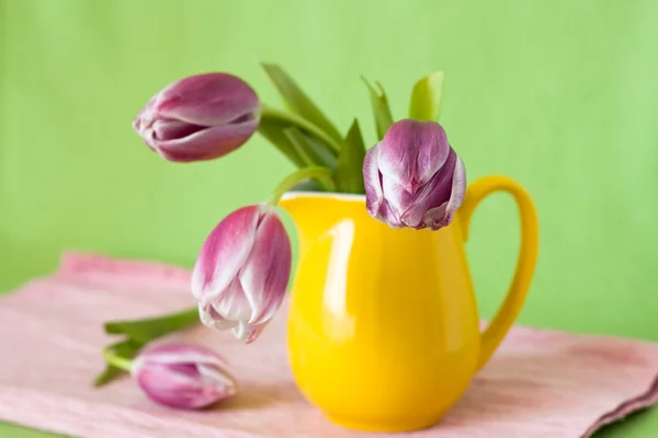 Delicate bouquet of purple tulips in a yellow jug — Stock Photo, Image