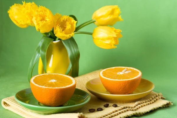Желтый кувшин с желтыми тюльпанами и сочными апельсинами на завтрак — стоковое фото